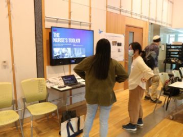 Shannon Li stands by a large monitor that displays the project, "Nursing Skills."
